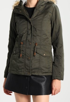 Giacca isolata verde oliva con cappuccio foderato in pelliccia sintetica, vita con coulisse, zip frontale e molteplici tasche. Texture liscia con dettagli di cucitura.