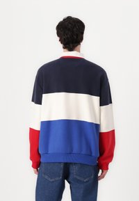 Farveblokeret sweatshirt i marineblå, hvid, rød og blå. Blødt stof, løstsiddende pasform, ribbede mansjetter og nederste kant. Bagview vist.