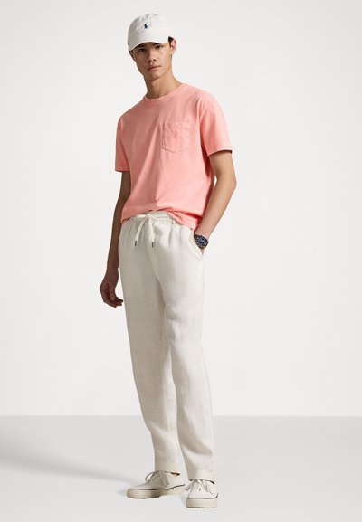 Coral pink short-sleeve T-shirt with a chest pocket, paired with cream-colored linen pants and white sneakers. Adjustable drawstring waistband.