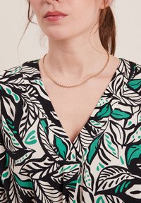 Haut à motif floral aux couleurs noire, verte et blanche. Design en V avec une texture douce et un délicat collier en chaîne dorée.