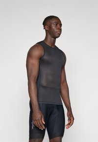 Schwarzes ärmelloses Sporttop aus strukturiertem Stoff, figurbetontes Design und gerippte Details. Kombiniert mit schwarzen Radhosen mit Logos.