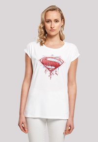 Weißes T-Shirt mit kurzen Ärmeln, das auf der Vorderseite ein rotes und blaues Superman-Logo mit verpixeltem Designdetails zeigt. Aus weichem Baumwollmaterial.