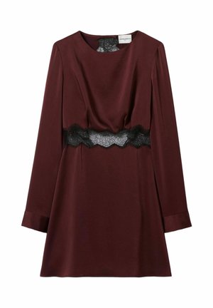 Mujer con vestido de manga larga color granate con cinturón de encaje negro, jersey amarillo sobre los hombros, zapatos con estampado de leopardo, calcetines grises y bolso granate en la mano.