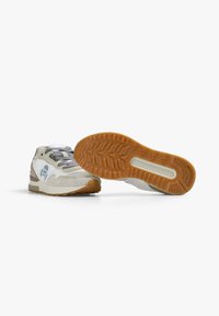 Zapatillas ligeras que combinan cuero blanco y gamuza beige, con cordones grises y una suela de goma marrón con un diseño de tracción.