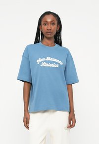 T-shirt de algodão azul claro com mangas curtas e gola redonda, apresentando letras em branco em destaque "New Balance Athletics" na parte da frente.