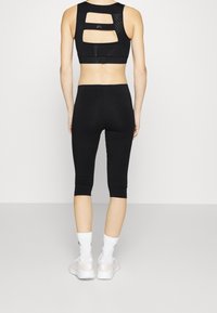 Black sports bra with open back design, paired with black capri leggings. Model wears white athletic shoes and socks. Smooth, stretchy fabric.