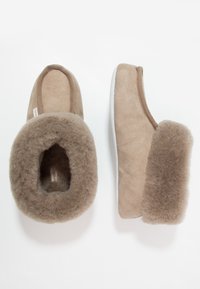 Brown suede slippers with a soft, fuzzy wool lining and thick soles. The design features a rounded toe and a fold-over cuff detail.