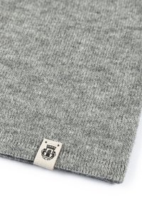 Knitted gray fabric with a soft texture, featuring a stitched beige label with a crest design at one corner, enhancing detail and branding.