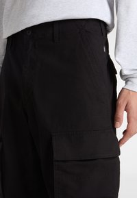 Zwarte cargobroek met een gladde textuur, zijzakken en een knoopsluiting. De tailleband is eenvoudig met riemlussen en zichtbare stiksels.