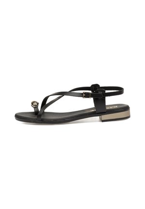 Sandalia plana negra con tiras delgadas, una parte del dedo en forma redondeada con un acento metálico y un tacón bajo cuadrado. Textura suave y diseño minimalista.