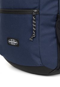 Mochila Eastpak azul marino con superficie texturizada, cremallera negra y tira tejida en el tirador, con base negra y parche con el logo.