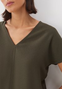 Maglietta verde oliva a scollo a V realizzata in tessuto morbido, con una sottile trama e maniche corte rifinite in modo pulito lungo il collo.