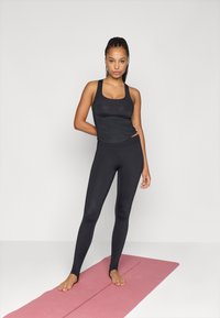 Μαύρη αθλητική φανέλα και κολάν με εφαρμοστό σχέδιο, λεία υφή και χωρίς ορατά σχέδια, τοποθετημένα σε ροζ γιόγκα μάτ.