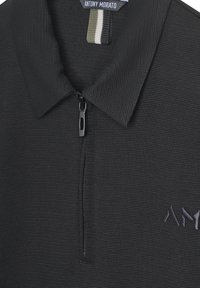 Camisa polo negra con cremallera, de textura acanalada, que cuenta con un cuello elevado, cierre de cremallera y un sutil logo bordado en gris oscuro.