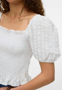 Top bianco con maniche a palloncino, scollatura quadrata, texture arricciata e orlo arricciato. Realizzato in tessuto leggero con sottili righe verticali.