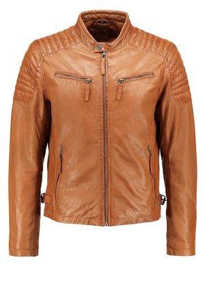 Mann trägt eine hellbraune Lederjacke, graues Hemd, schwarze Hose und schwarze Stiefel und steht mit einer Hand in der Tasche vor weißem Hintergrund.