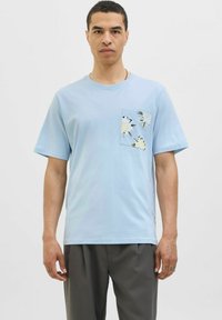 Lyseblå bomulds-T-shirt med korte ærmer og en brystlomme med et blomsterprint i sort og creme. Glat tekstur, afslappet pasform.