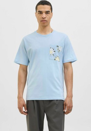 T-shirt en coton bleu clair avec des manches courtes et une poche poitrine ornée d'un motif floral en noir et crème. Texture lisse, coupe décontractée.