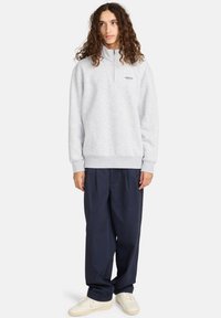 Lichtgrijze sweatshirt met een half-rits kraag, elastische manchetten en zoom, gecombineerd met losse marineblauwe broek en crèmekleurige sneakers.