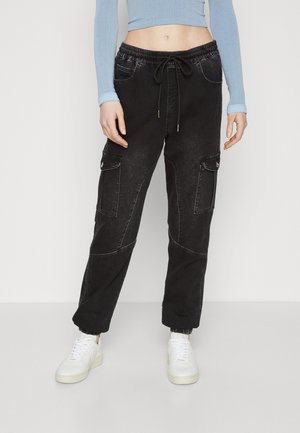 Svarte cargobukser med elastisk midje, snøring og flere sidelommer. Har en falmet tekstur og mansjettkant. Kombinert med hvite sneakers.