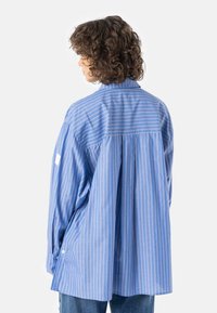 Blå og hvitstripet oversized skjorte med knappet krage, senkede skuldre og detaljer med plissering bak, laget av lett stoff.