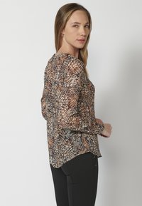 Blusa trasparente con maniche lunghe, caratterizzata da un motivo di fogliame astratto multicolore. Presenta un collo rotondo e un orlo leggermente curvato.