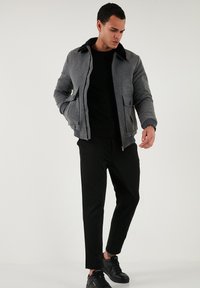 Sivý bomber s čiernym golierom, s dvoma prednými vreckami, so žebrovanými manžetami, nosený cez čierne tričko a skombinovaný s čiernymi slim-fit nohavicami a teniskami.