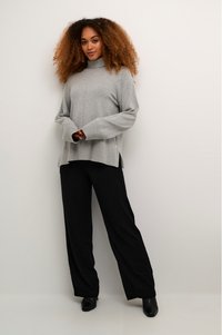 Grauer Rollkragenpullover mit geripptem Textur, Seitenschlitzen und langen Ärmeln, kombiniert mit lockeren schwarzen Hosen und schwarzem Schuhwerk.