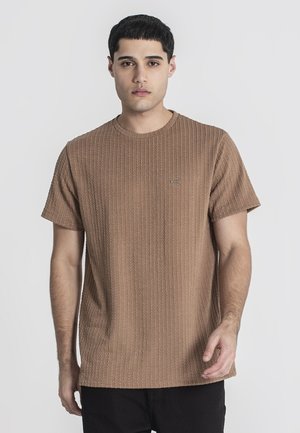 Braunes T-Shirt mit strukturiertem Material, geripptem Muster, rundem Halsausschnitt und kurzen Ärmeln. Kleines Logo-Patch nahe der linken Schulter.