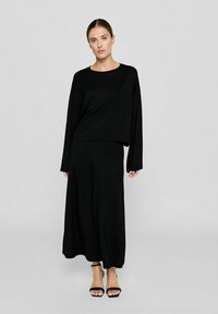 Schwarzes Zweiteiler-Outfit bestehend aus einem langärmligen Oberteil mit lockerem Schnitt und einem Midikleid. Hergestellt aus weichem, glattem Stoff.