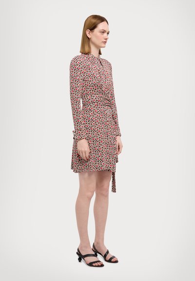 Robe à motifs rouges et blancs avec des manches longues, design enveloppant et ourlet asymétrique. Assortie à des sandales noires à lanières.