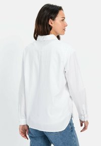 Chemise blanche à manches longues avec col, dotée d'une texture de tissu lisse et de poignets à bouton, assortie à un jean en denim bleu.