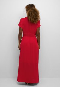 Robe maxi rouge à manches courtes, avec des plis texturés et une taille élastique. Tissu lisse qui tombe jusqu'aux chevilles.