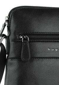 Borsa a tracolla nera in pelle con superficie texturizzata, dotata di tasca frontale con zip e accessori in argento. Il nome del marchio è impresso sulla parte anteriore.