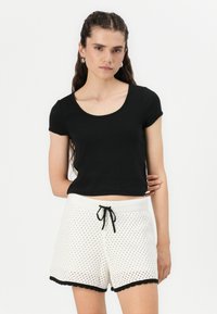 Black cropped t-shirt with short sleeves paired with white mesh shorts featuring a black scalloped hem and adjustable drawstring waist.