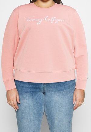 Pink sweatshirt with a crew neckline, long sleeves, and a white embroidered logo on the front. Paired with light blue distressed jeans.