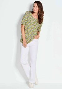 Korte mouwen groene en gele bloemenprint blouse met een ronde hals, gecombineerd met witte rechte broek en lichtgekleurde sneakers.