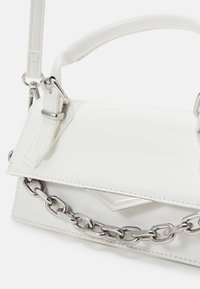 Vit fusk läderhandväska med en strukturerad design, silverfärgad hårdvara, kedjedetalj och ett handtag ovanpå. Slät textur och minimalistiska accenter.