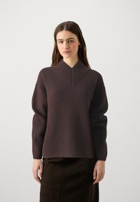 Pruun kudumisse sweater, millel on ribitud V-kaelus ja langenud õlaõmblused, sobivad tumeda seeliku juurde. Omab pehmet tekstuuri ja lõdva istuvust.