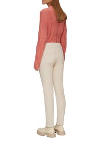 Pull en tricot rose clair, pantalon beige taille haute, et bottines beige. Le pull présente un motif texturé ; le pantalon a des poches arrière.