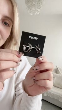 Sidabrinės metalinės lankelio ir smeigtuko auskarai ant DKNY dizaino kortelės. Lankelyje yra tinklo raštas, o smeigtukas turi stačiakampį dizainą.