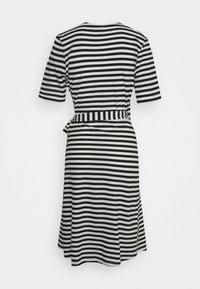 Raitapaita mustavalkoisena, lyhyillä hihoilla, istuvalla vyötäröllä ja solmittavalla yksityiskohdalla, joka virtaa tyrskähikeen, valmistettu pehmeästä kankaasta.