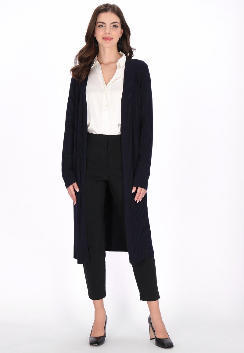 Cardigan lung, bleumarin, cu dungi, din țesătură tricotată, asortat cu o cămașă albă și pantaloni negri. Textură netedă și design cu fața deschisă.