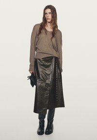 Brun strikket sweater, sort læder omslagsskjørt med snapdetalje, parret med knæhøje sorte støvler og en lille sort clutch.