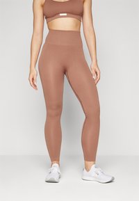 Braune, gerippte, hochtaillierte Leggings aus elastischem Material, kombiniert mit einem passenden Crop-Top und weißen Sportschuhen.