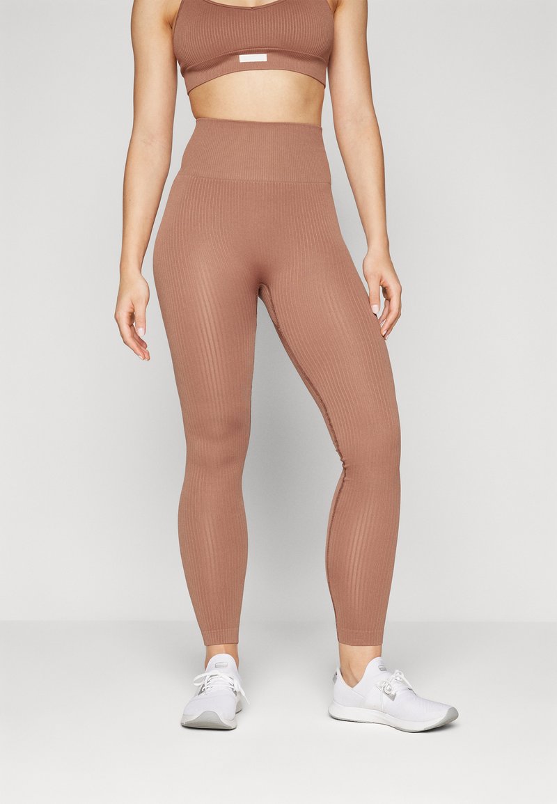 Braune, gerippte, hochtaillierte Leggings aus elastischem Material, kombiniert mit einem passenden Crop-Top und weißen Sportschuhen.