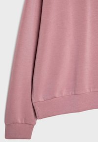 Manche et ourlet de sweat-shirt rose à manches longues avec poignets côtelés et texture de tissu lisse sur fond clair.