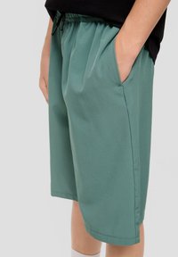 Grüne Shorts aus weichem Stoff, mit einem elastischen Bund und Kordelzug, seitlichen Taschen und einem lockeren Schnitt.