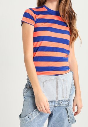 Kortærmet, tætsiddende t-shirt med vandrette orange og blå striber. Kombineret med højttaljede lyseblå denim-velcro-bukser.