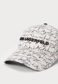 Weißer Baseballcap mit einem schwarzen handgeschriebenen Muster und gesticktem "Karl Lagerfeld"-Text auf der Vorderseite. Gebogener Schirm, verstellbarer Rücken.
